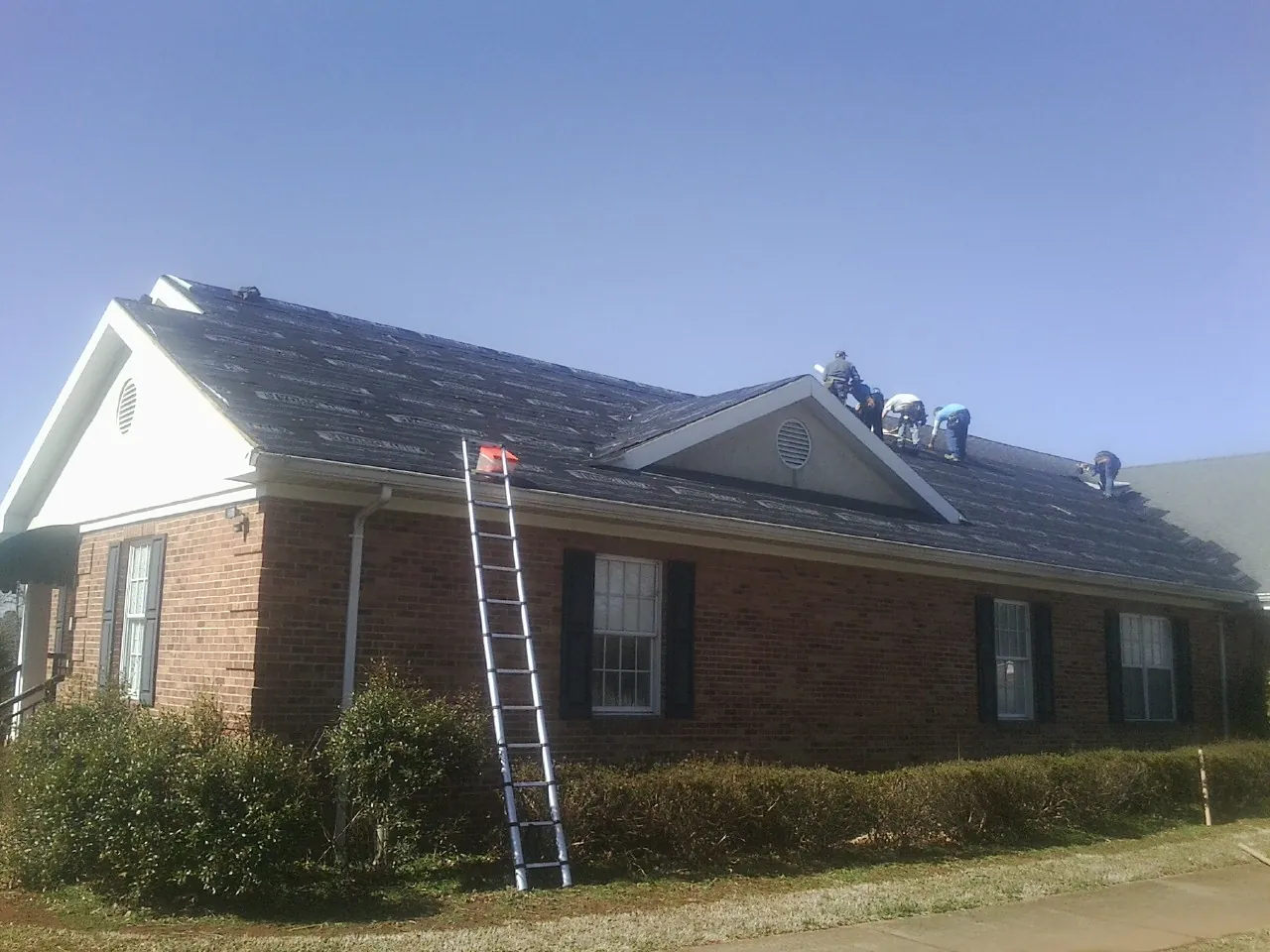 Crew tearing shingles off a brick ranch roof with a ladder set — Metal Roof Repair work by our crew in New Plymouth